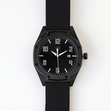 Front view of the LUQ Black Stainless Steel Watch with a matte black 45mm case, black dial, and silicone strap. The luminous numerals and hands enhance visibility in low light.