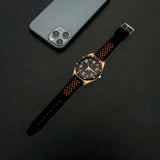 Elegant men's watch with rose gold details and black strap, alongside a smartphone on a dark surface