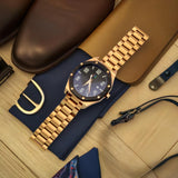 Designer rose gold men's watch on a navy blue tie, paired with stylish leather accessories.