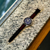 Designer men's watch with a sporty red and black strap, laid on a marbled surface.