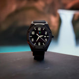 Close-up view of a men's black designer watch with a sleek, modern design, set against a soft-focused background.